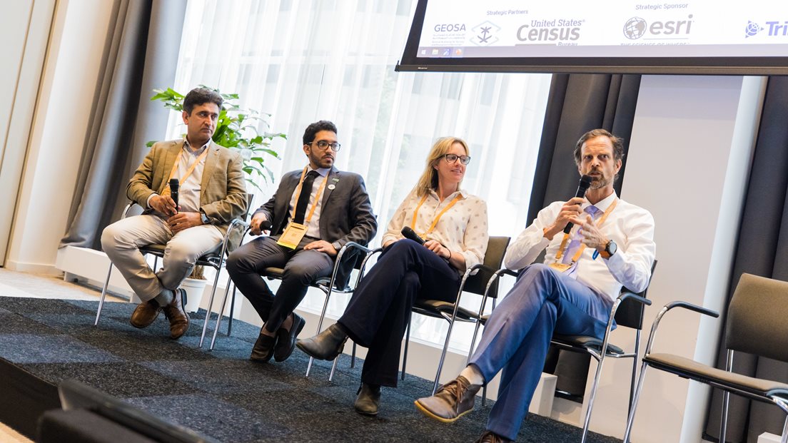 Fire menneske sit på kva sin stol på ei scene. Ein av dei snakkar i ein mikrofon. Foto: Geospatial World Forum