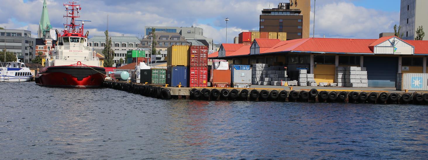 Kaianlegg i Kristiansand havn med konteinere og paller med varer på kaikanten, båter til venstre