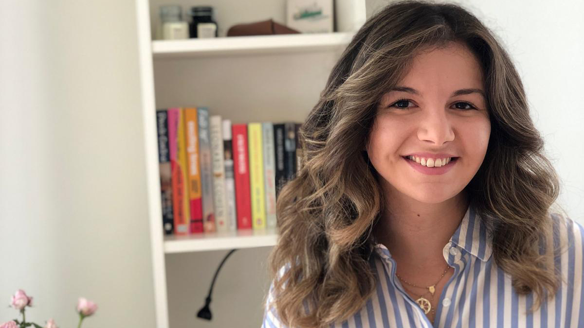 Dame med langt m&oslash;rkt h&aring;r og bl&aring;stripete skjorte smiler.