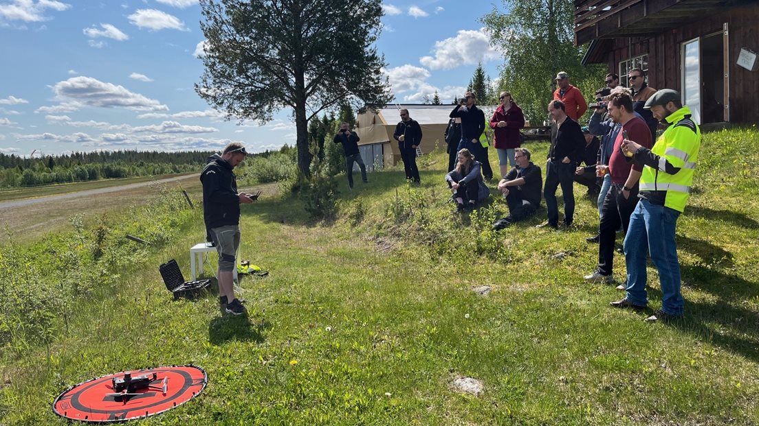 Flere personer står og ser på en mann som ska fly drone