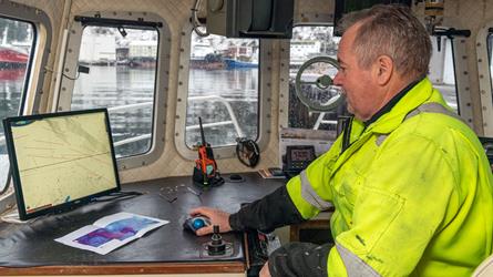 Yrkesfisker sitter i om bord i fiskebåt og ser på kart i sin kartplotter. Foto.