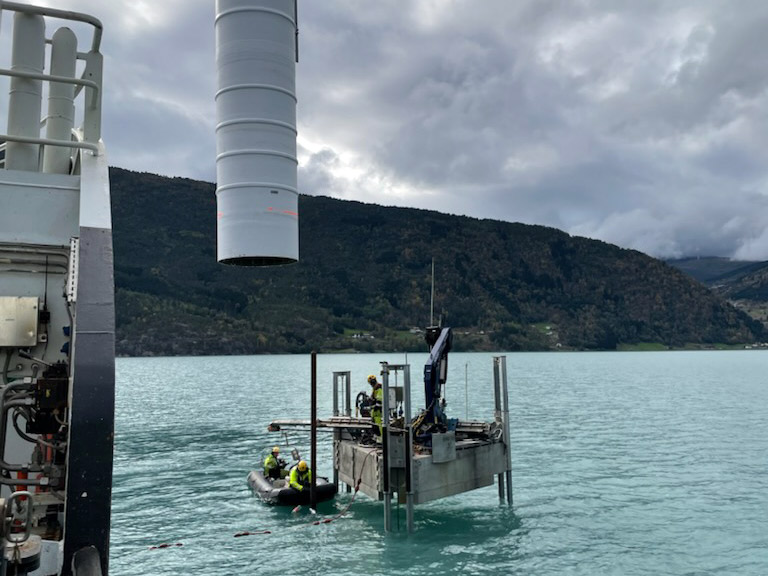 Sj&oslash;merke installeres til sj&oslash;s. En mann st&aring;r p&aring; installasjonen mens to menn hjelper til fra gummib&aring;t. Deler av skip ses i forgrunnen. Foto: Kystverket