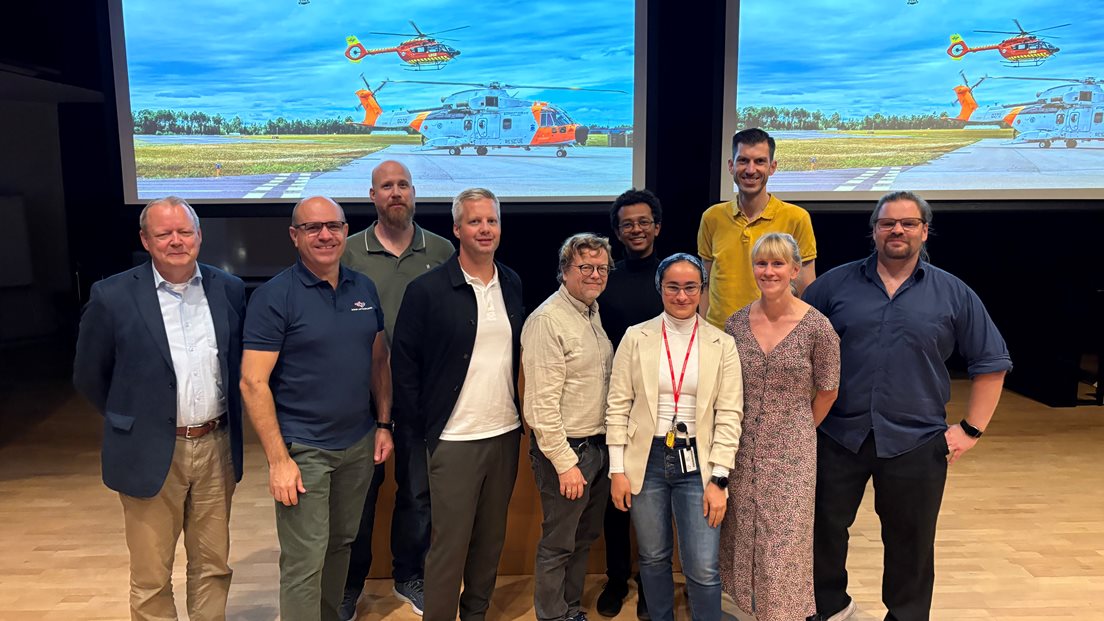 Ti menneseker samla på en scene foran to storskjermer som viser beredskapshelikopter.