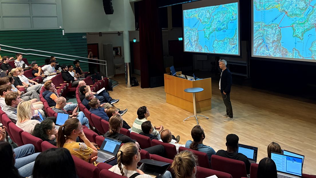 Mannlig fylkeskartsjef foran forsamling med studenter som ser på et kart på storskjerm.