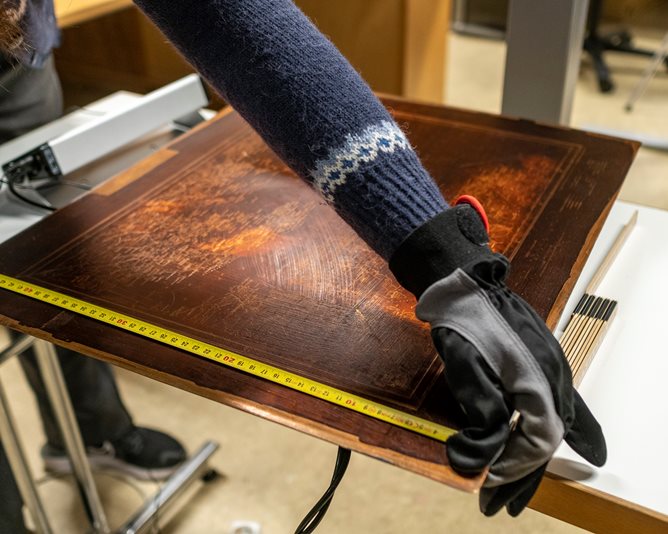 Trykkplate i kobber blir veid og målt med målebånd.