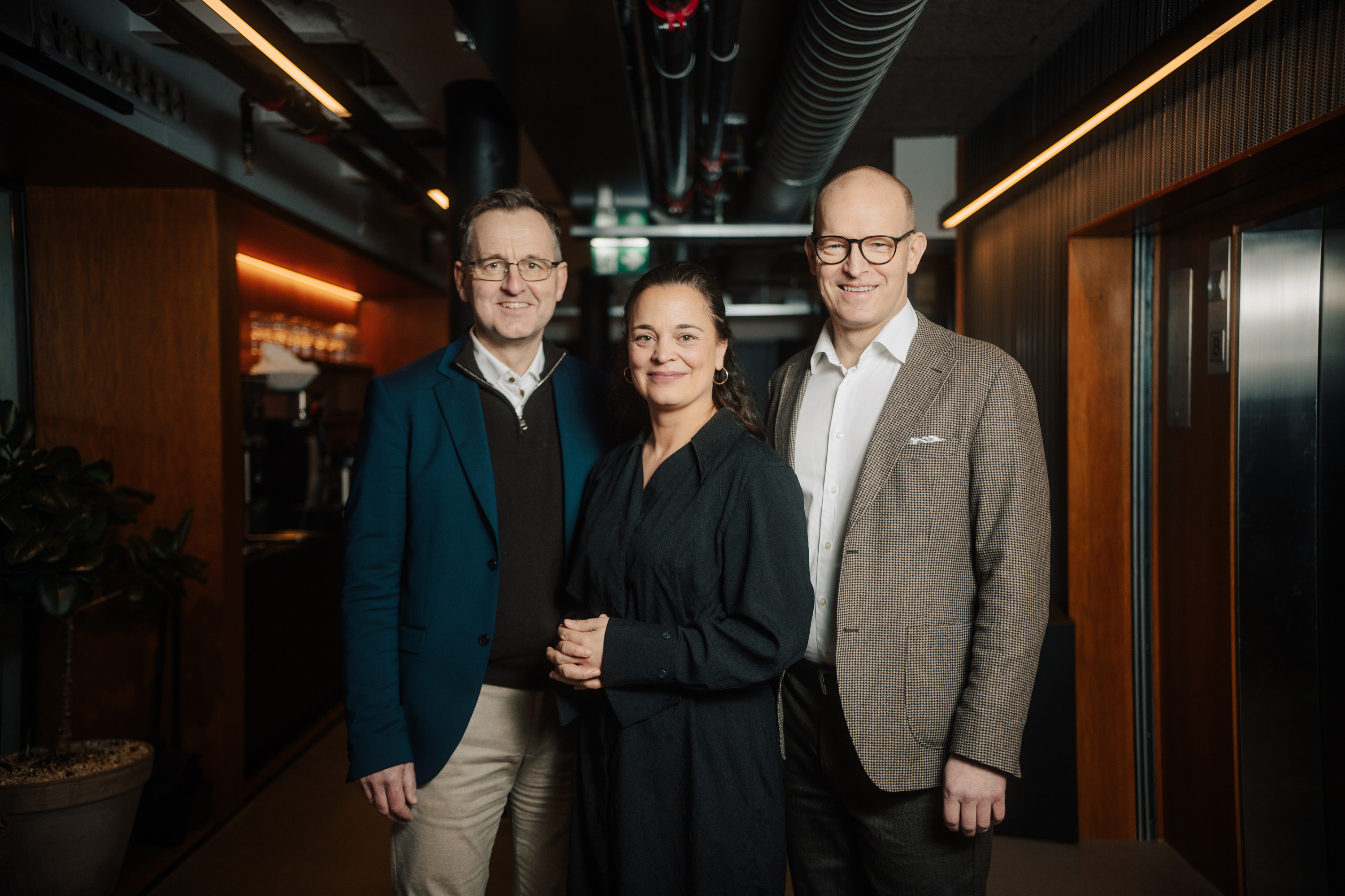 To menn og ei kvinne smiler mot kamera i et halvmørkt