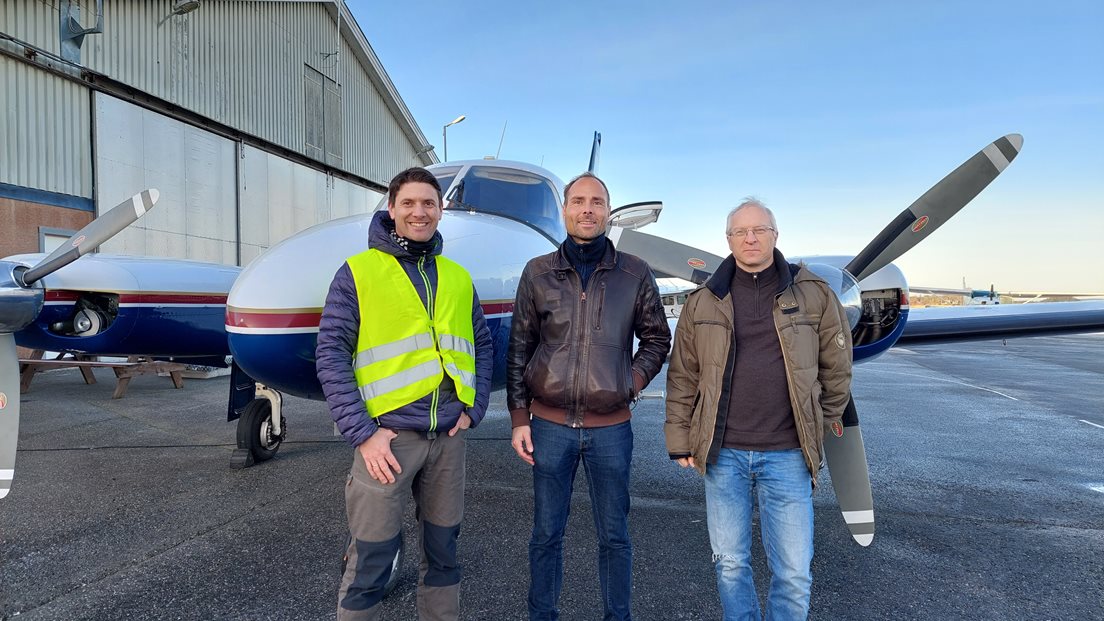 Tre personer foran et småfly på en flyplass.