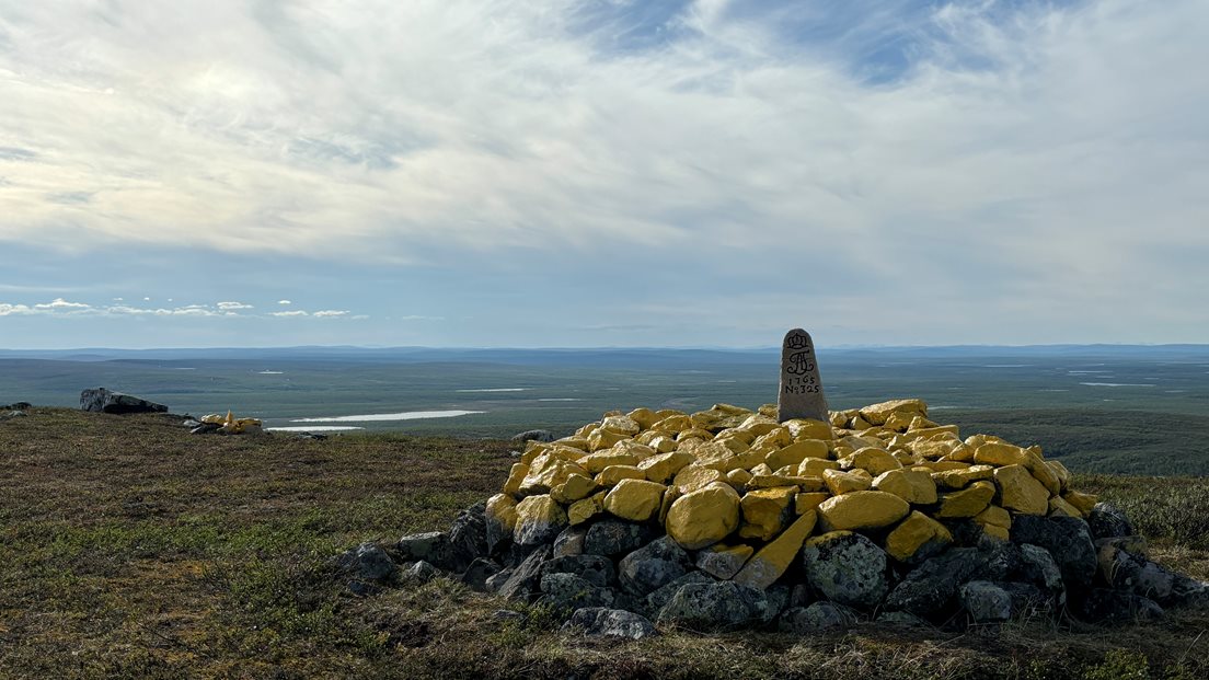 Riksrøys 325 markerer den norsk-finske grensen. Stabel av gule steiner med en grensemarkør på toppen, omgitt av åpne landskaper.