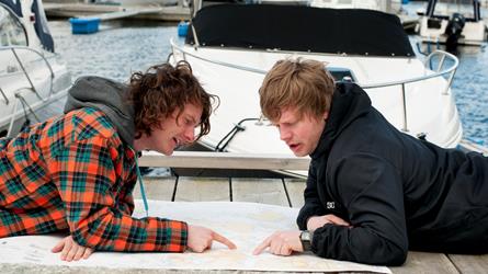 To yngre menn ligger på brygga i ei småbåthavn og peker i et papirsjøkart. Foto: Morten Brun