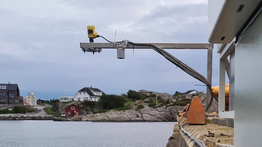 Permanent vannstandmåler er montert på ei kai i Sirevåg på Jæren. Utsikt utover sjøen og bebyggelse på andre siden. Foto: Bjørn Erik Bue