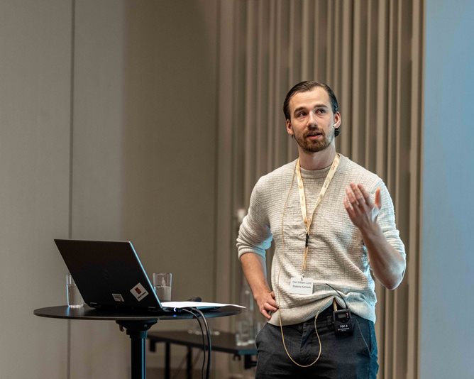 Mannlig kartverksansatt Carl William Lund viser taktile kart på Geomatikkdagene 2025