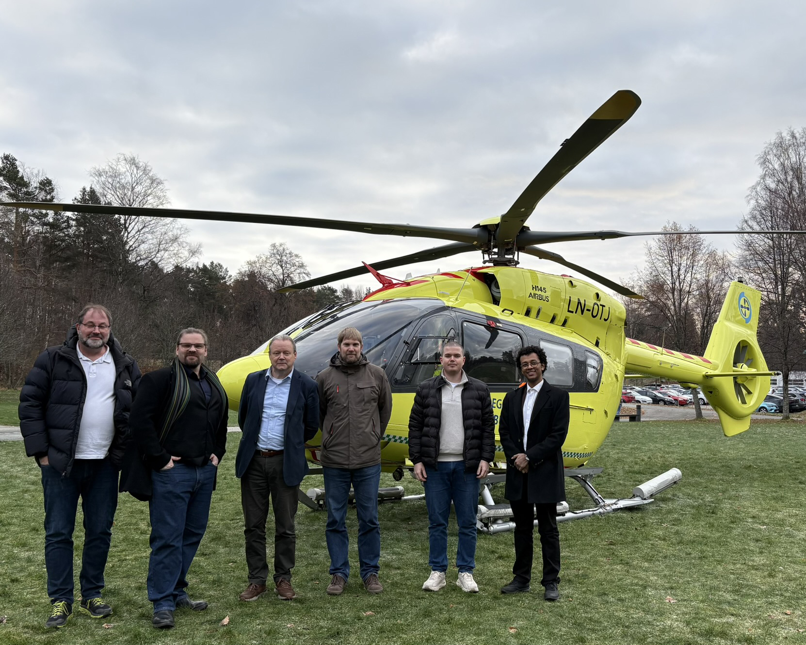 En gruppe menn foran parkert helikopter fra Luftambulansen.